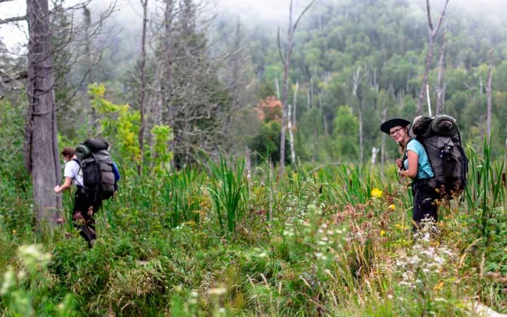 a group of students backpack through a grassy clearing on a gap year expedition with outward bound 